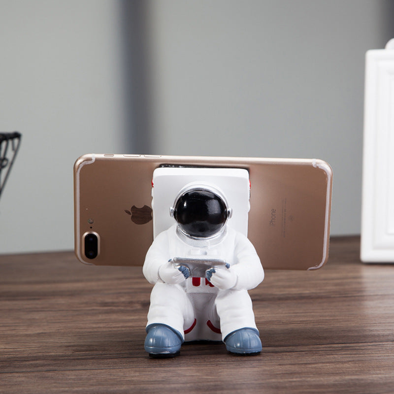 Decoratieve telefoonhouder in de vorm van een zittende astronaut, wit met zwarte helm en tablet in handen