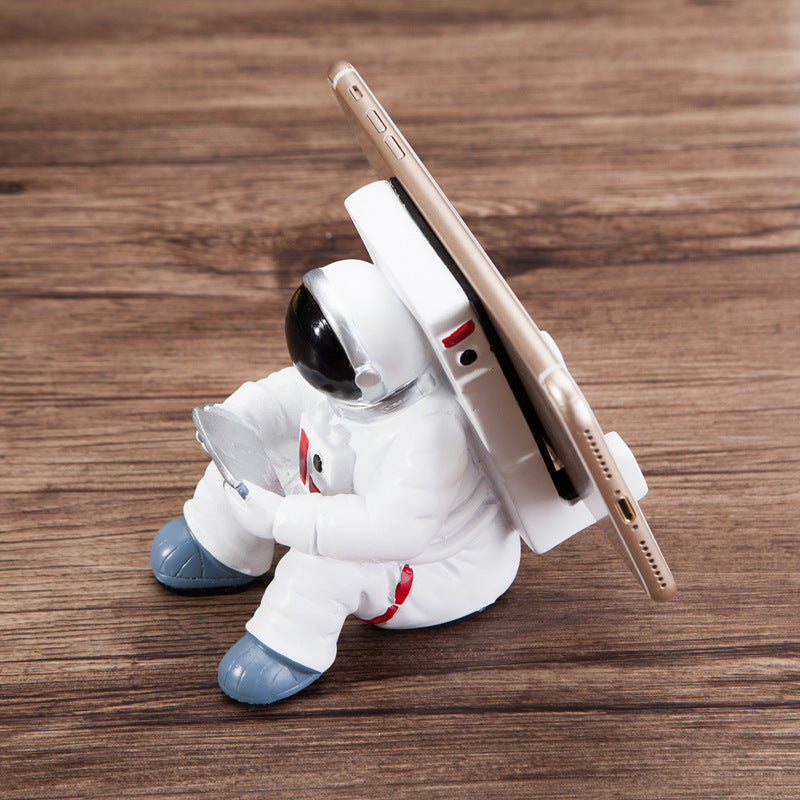 Decoratieve telefoonhouder in de vorm van een zittende astronaut, wit met zwarte helm en tablet in handen
