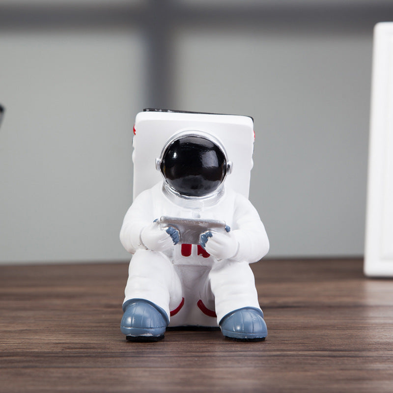 Decoratieve telefoonhouder in de vorm van een zittende astronaut, wit met zwarte helm en tablet in handen