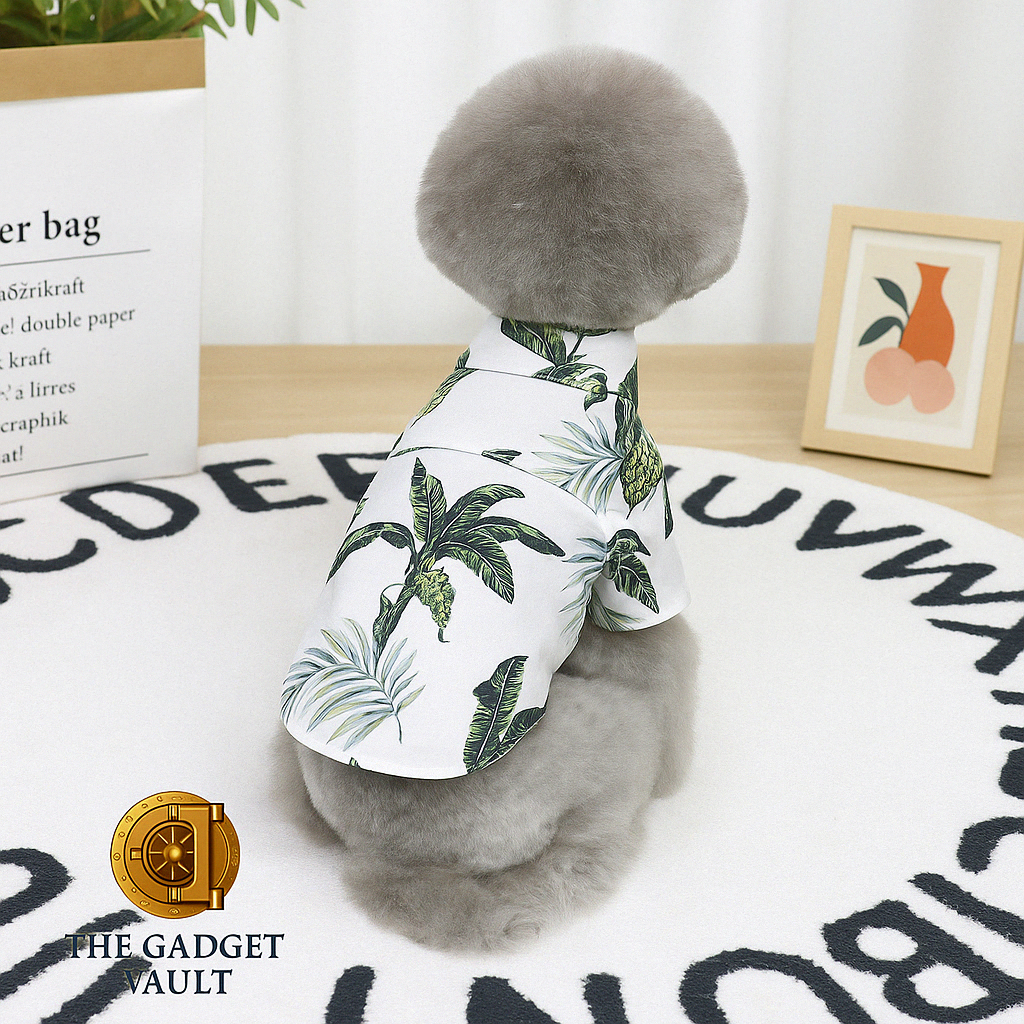 Een grijze poedel met pluizige vacht gefotografeerd van achteren, zittend op een wit vloerkleed met alfabetprint en gekleed in een wit Hawaiian-stijl hondenshirt met tropische bladeren, met subtiel The Gadget Vault-logo linksonder.
