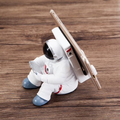 Decoratieve telefoonhouder in de vorm van een zittende astronaut, wit met zwarte helm en tablet in handen