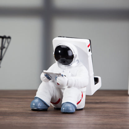 Decoratieve telefoonhouder in de vorm van een zittende astronaut, wit met zwarte helm en tablet in handen