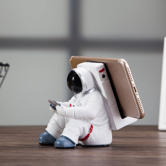 Decoratieve telefoonhouder in de vorm van een zittende astronaut, wit met zwarte helm en tablet in handen