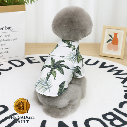 Een grijze poedel met pluizige vacht gefotografeerd van achteren, zittend op een wit vloerkleed met alfabetprint en gekleed in een wit Hawaiian-stijl hondenshirt met tropische bladeren, met subtiel The Gadget Vault-logo linksonder.