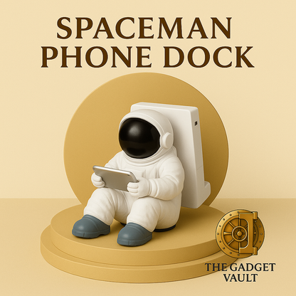 Decoratieve telefoonhouder in de vorm van een zittende astronaut, wit met zwarte helm en tablet in handen, geplaatst op een goud-beige achtergrond met het logo van The Gadget Vault rechtsonder.